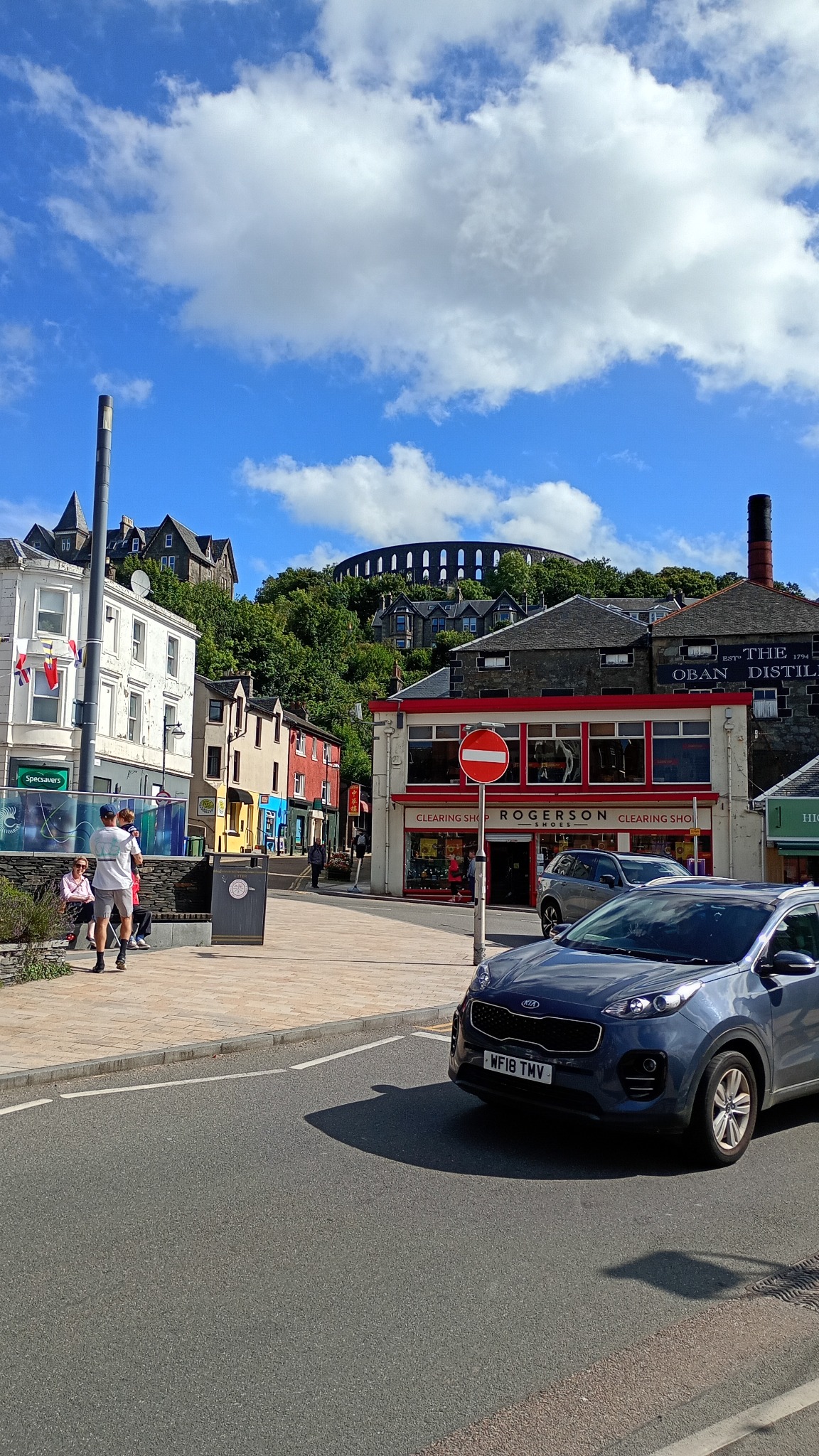 A sunny street in Oban with McCaig's Tower visible above the town